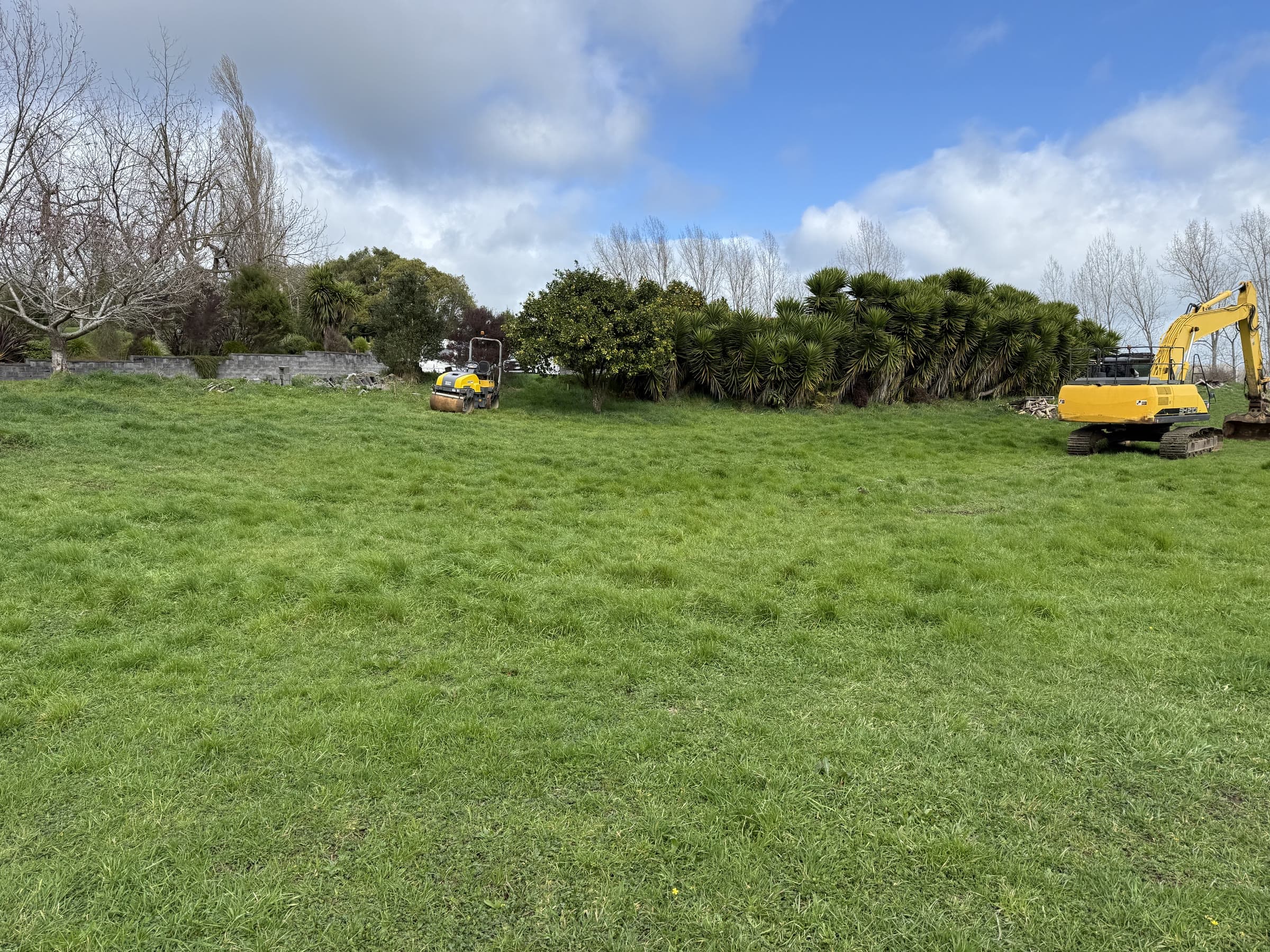 Yellow digger and roller on a grassed rural section before the work starts