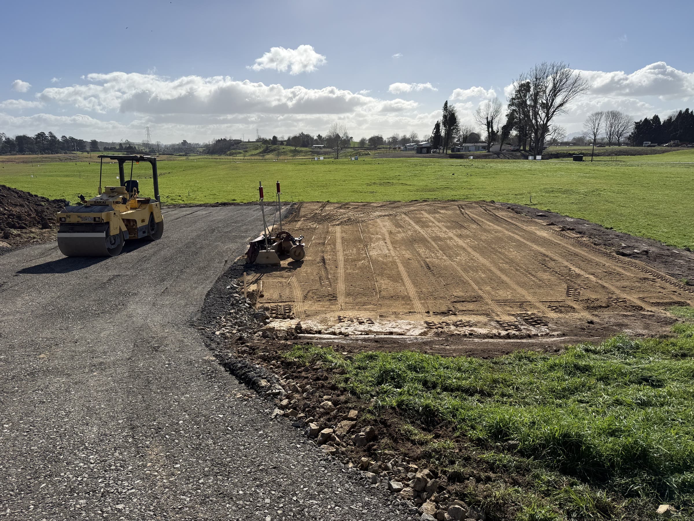 Roller and laser level beside a freshly compacted building pad and new metal driveway