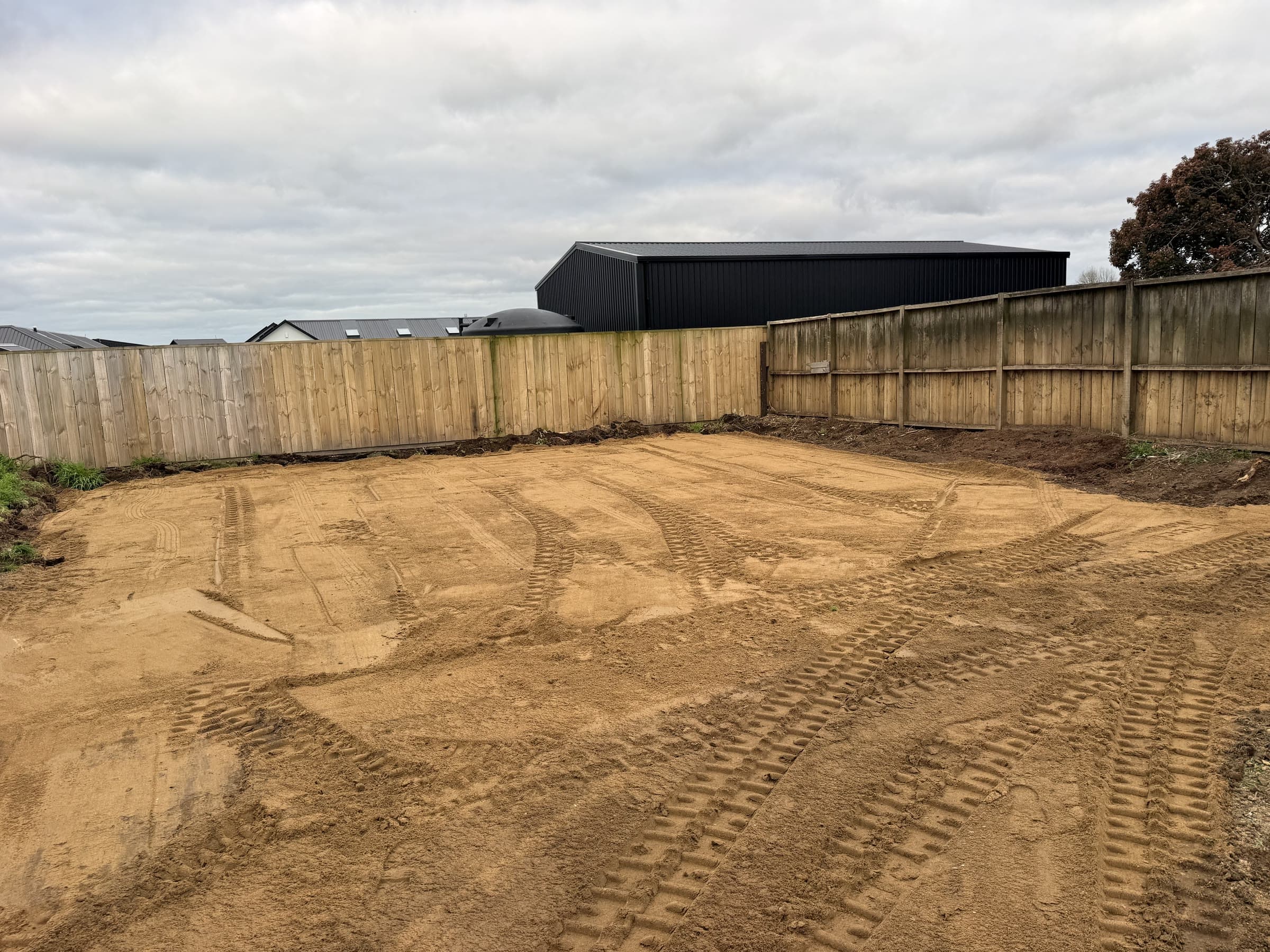 Levelled and compacted house site behind a timber boundary fence, track marks across the sand