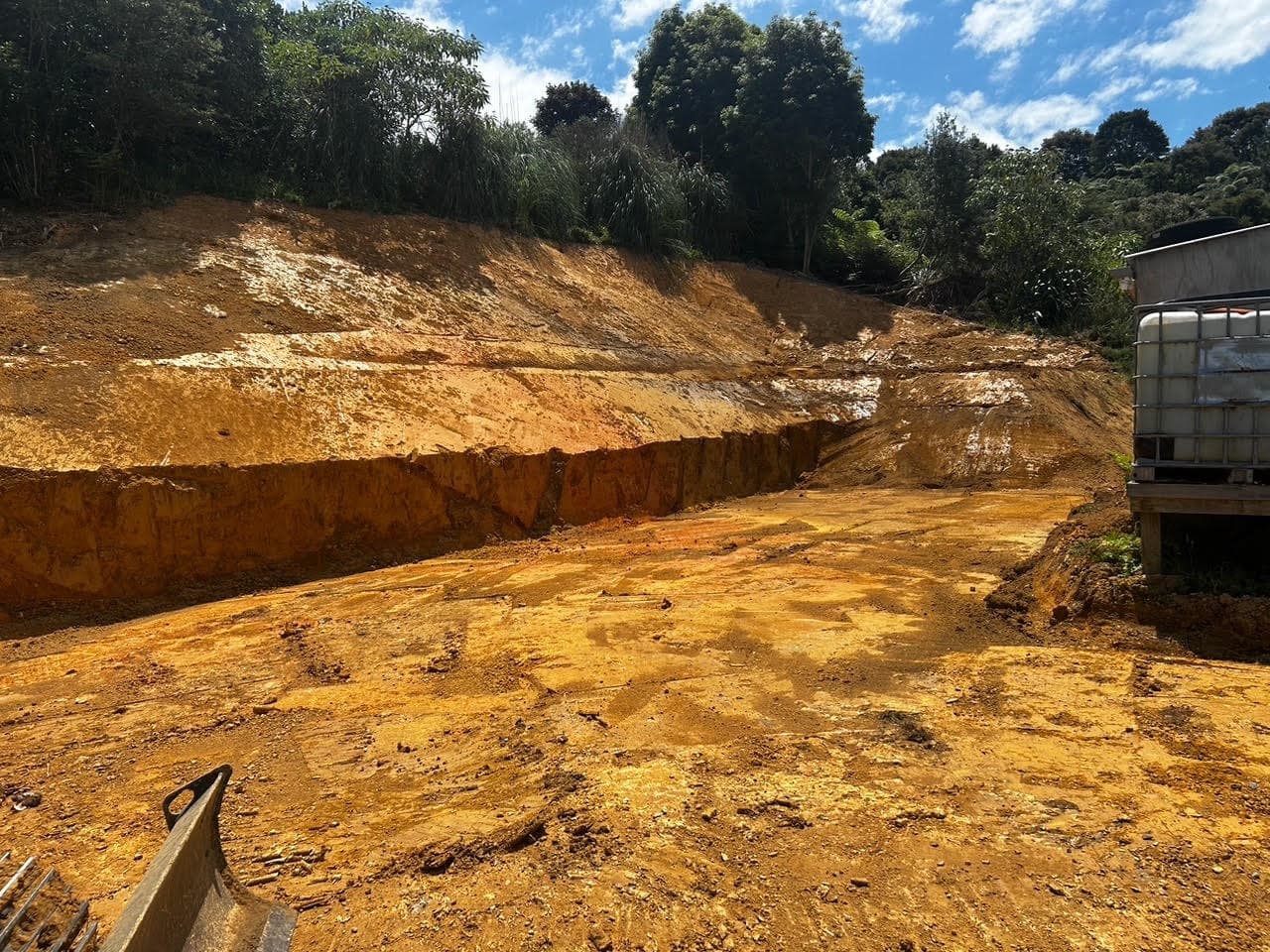 Flat building platform cut into a clay bank, a tall clean face left behind it