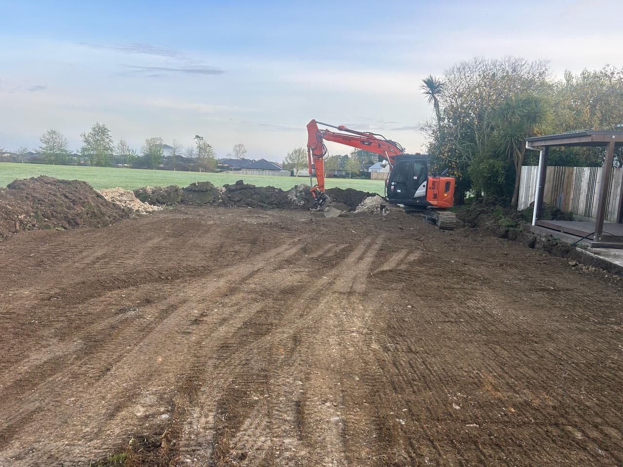 The same section stripped back to dirt, digger working at the far end with spoil heaped along the edge